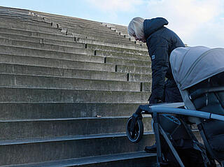 Zwei Personen tragen einen Kinderwagen eine Treppe hinauf