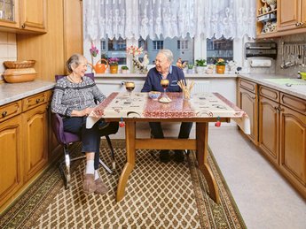 Innenaufnahme: Ein älteres Ehepaar sitzt am Küchentisch.
