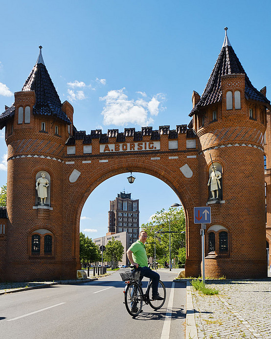 Heiner von Marschall hält vor dem Borsigtor, dem Eingang zum neuen Industriegelände. Der Fahrradweg führt an Berlins erstem Hochhaus vorbei, dem Borsigturm (hinten im Bild)