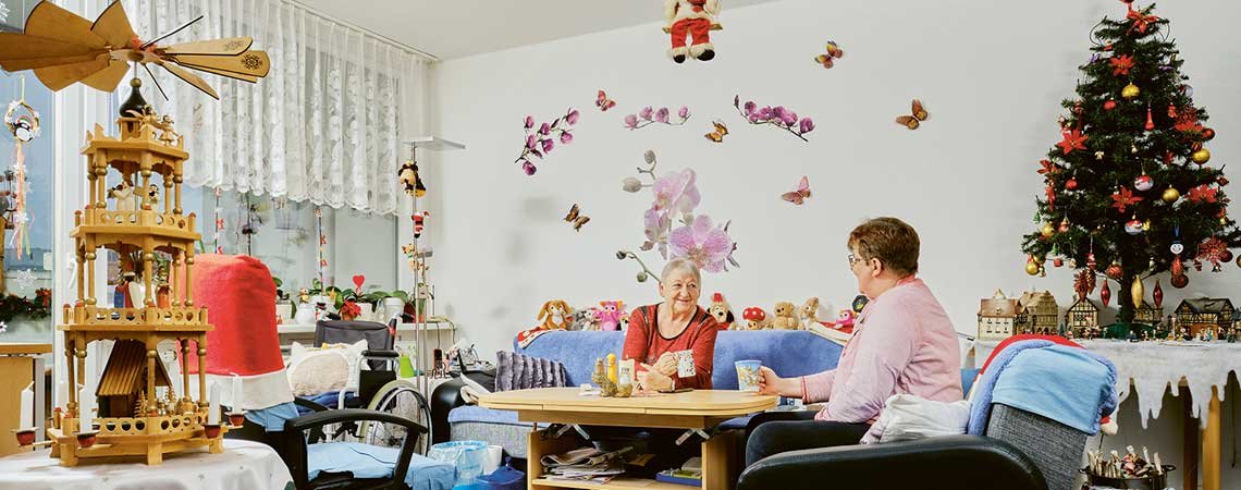 Innenaufnahme: Zwei Frauen sitzen in einem weihnachtlich geschmückten Wohnzimmer.