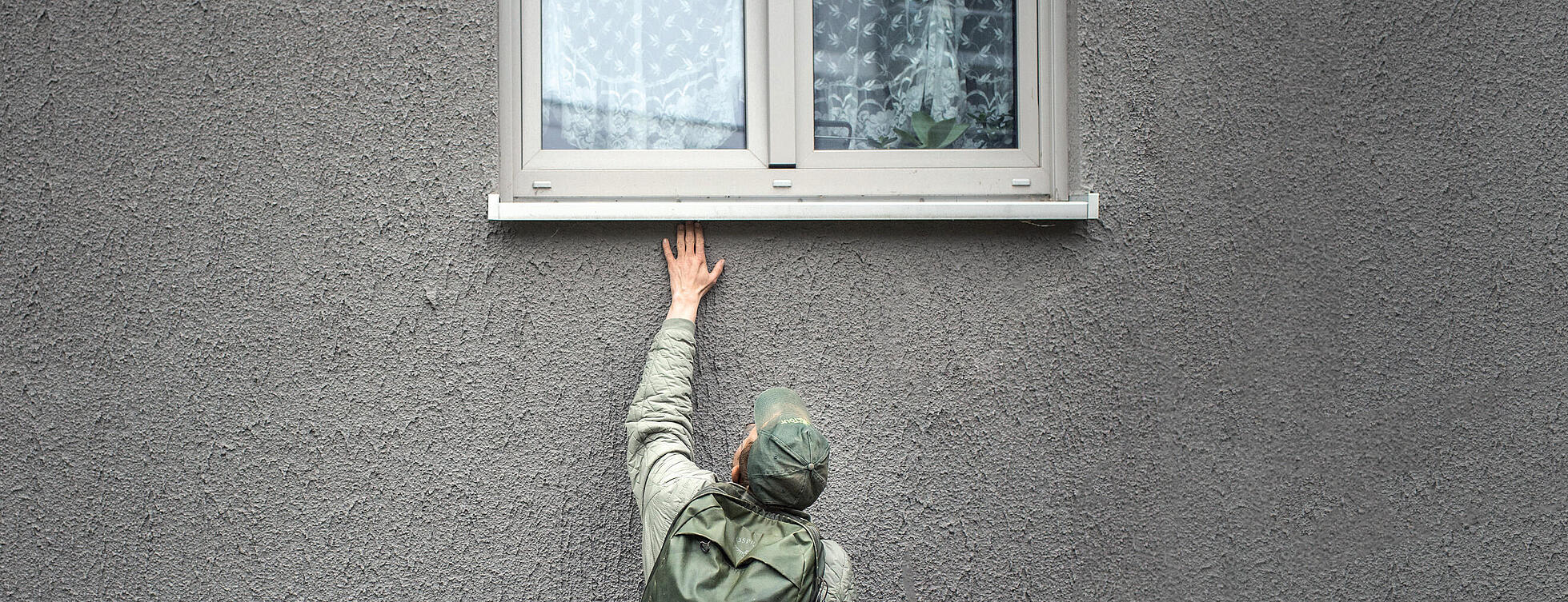 Mann greift unter eine Fensterbank auf der Suche nach einer Spinne