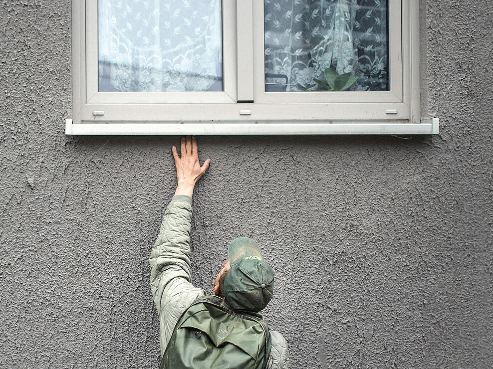 Mann greift unter eine Fensterbank auf der Suche nach einer Spinne