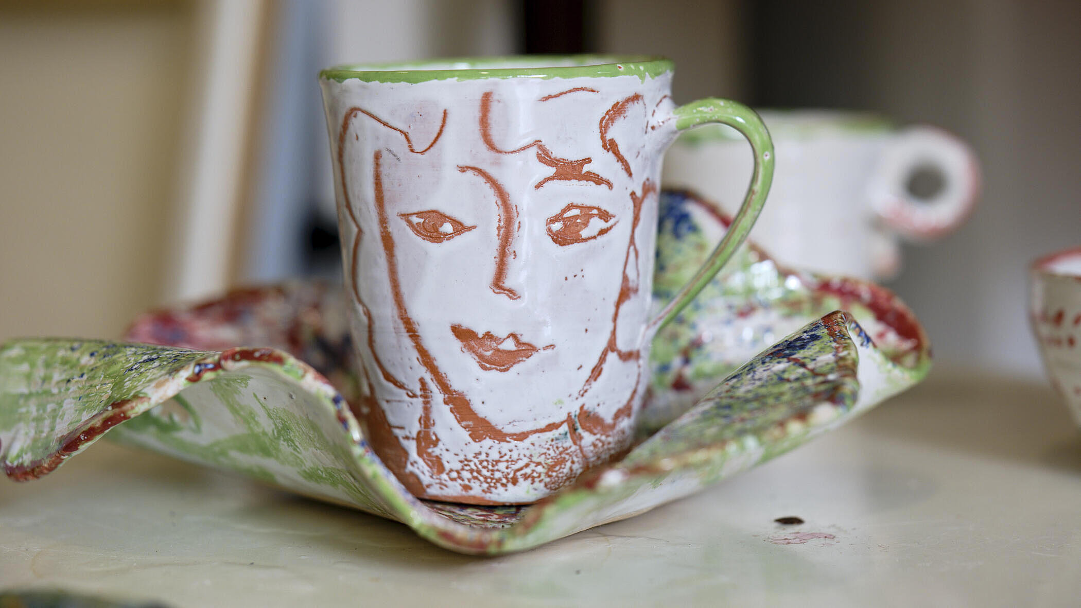 Eine Tasse aus Keramik mit gezeichnetem Gesicht auf einem wellenden Untersetzer