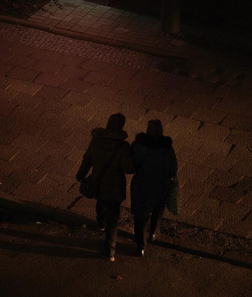 Zwei Personen überqueren eine beleuchtete Straße