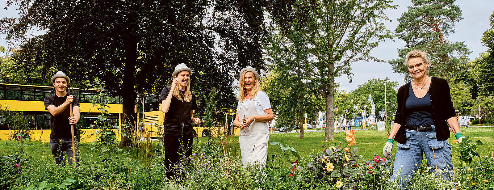 Außenaufnahme: Vier Personen bei der Gartenarbeit in einem Blumenbeet, im Hintergrund ein gelber Bus