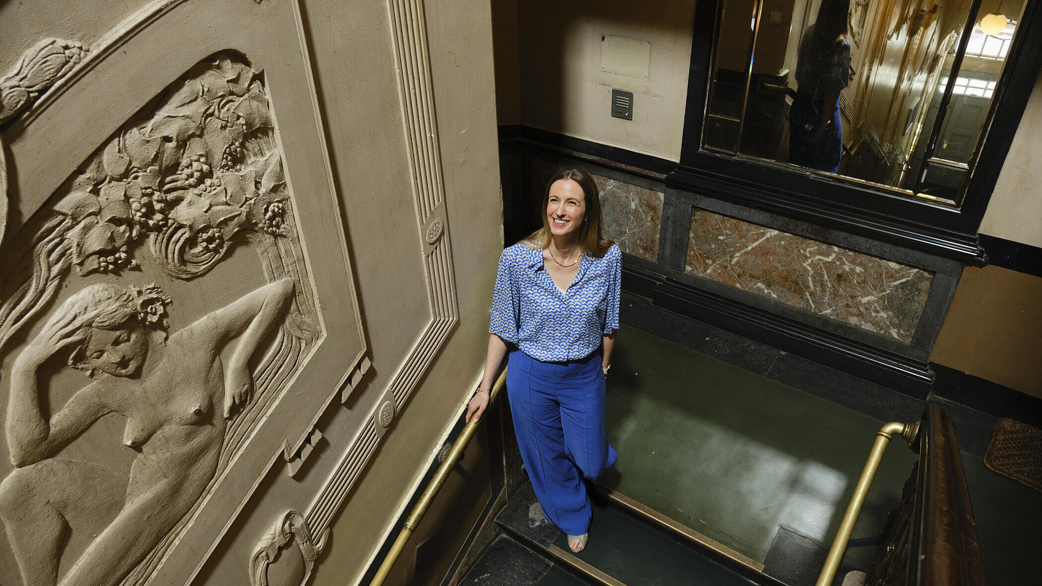 Katharina Basedow steht in einem stuckverzierten Treppenhaus.