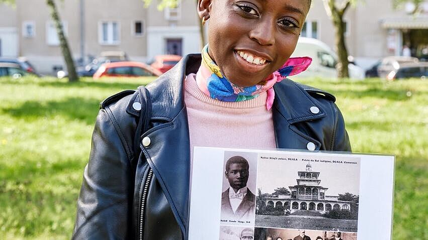 Außenaufnahme: Justice Mvemba zeigt auf Schwarz-Weiß-Fotos