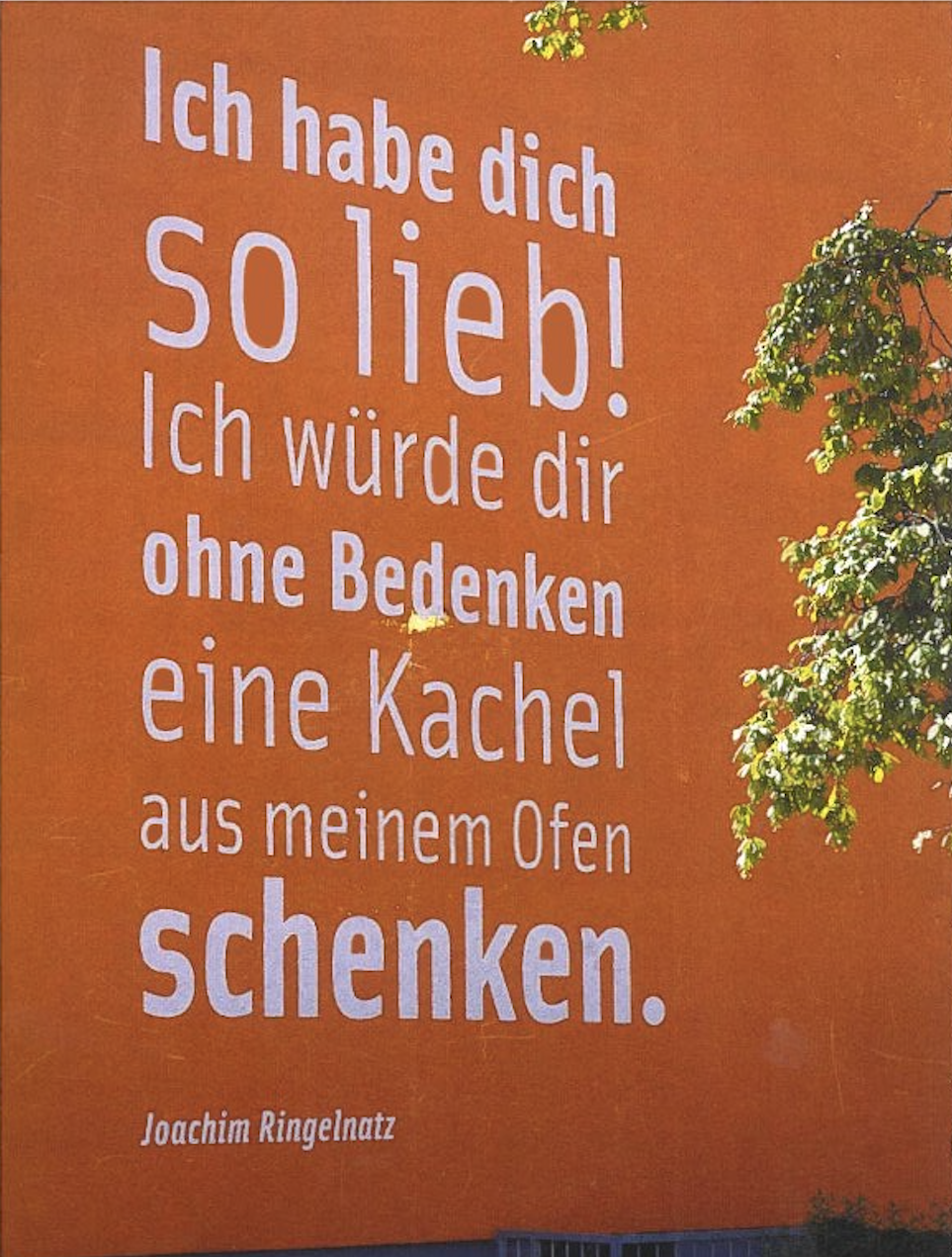 Eine Postkarte mit Blick auf eine Hauswand mit Aufschrift "Ich habe dich so lieb! Ich würde dir ohne Bedenken eine Kachel aus meinem Ofen schenken. -Joachim Ringelnatz"
