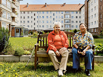 Zwei Frauen sitzen auf einer Bank vor den denkmalgeschützten Häusern des Schrammblocks