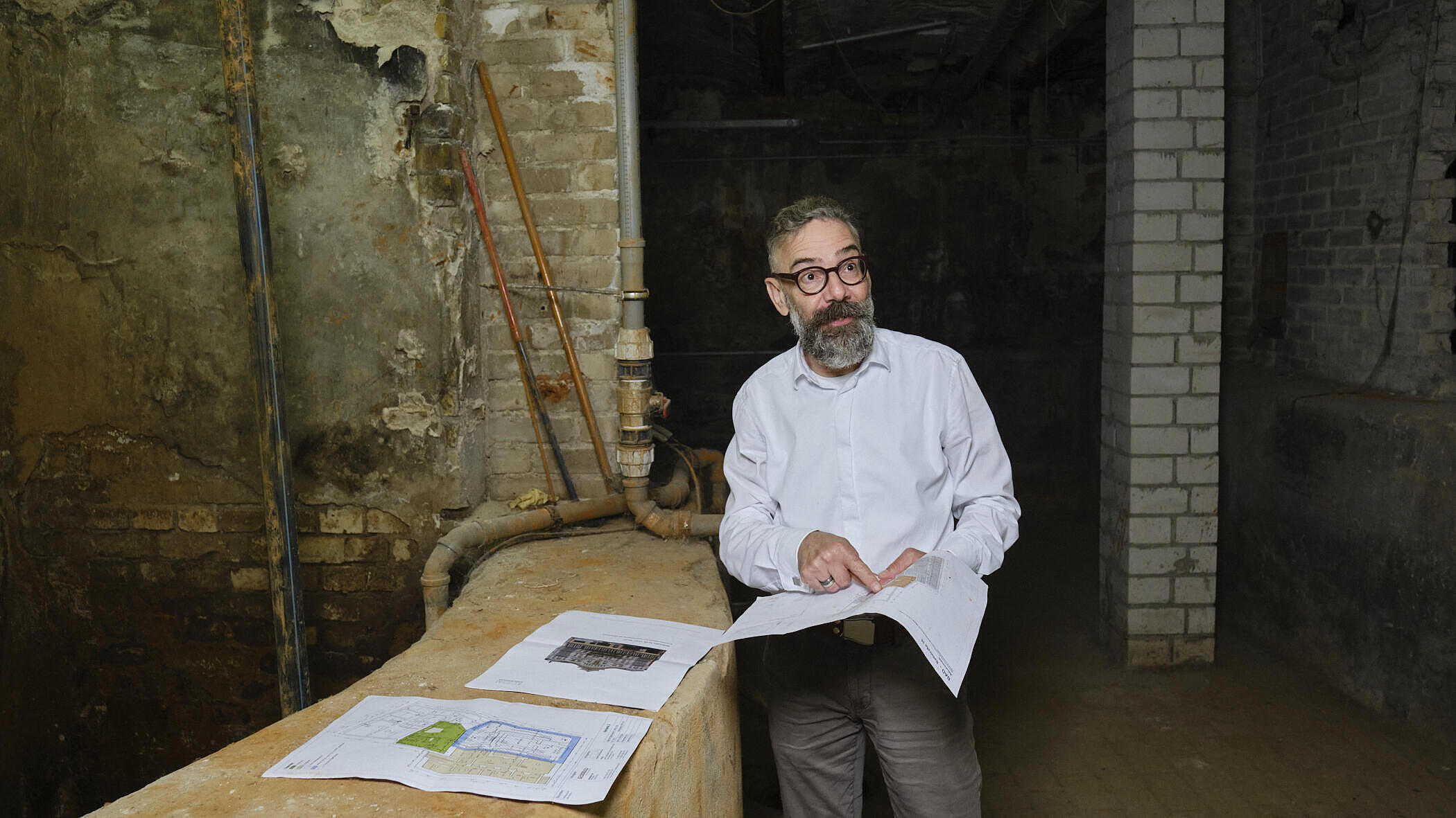 Yorck Höpfner steht in einem historischen Kellergewölbe und deutet auf einen ausgebreiteten Grundriss.