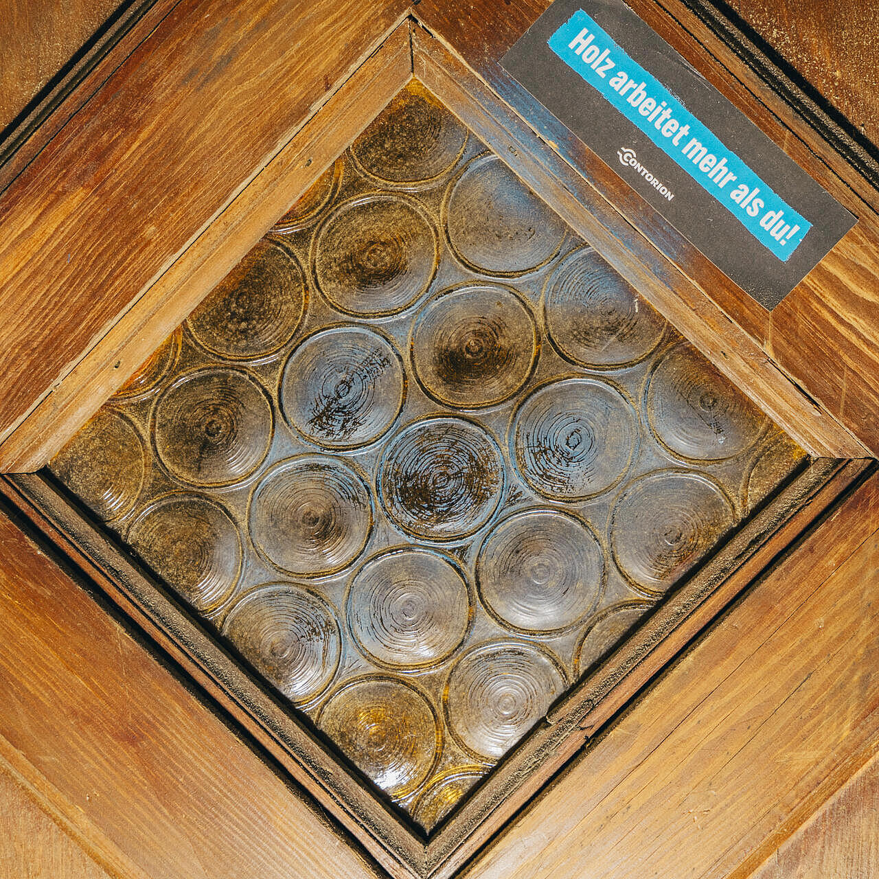 Eine Holztür mit Fenster und Sticker "Holz arbeitet mehr als du!"