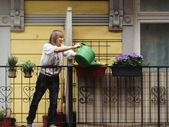 Frau gießt auf Balkon Blumen