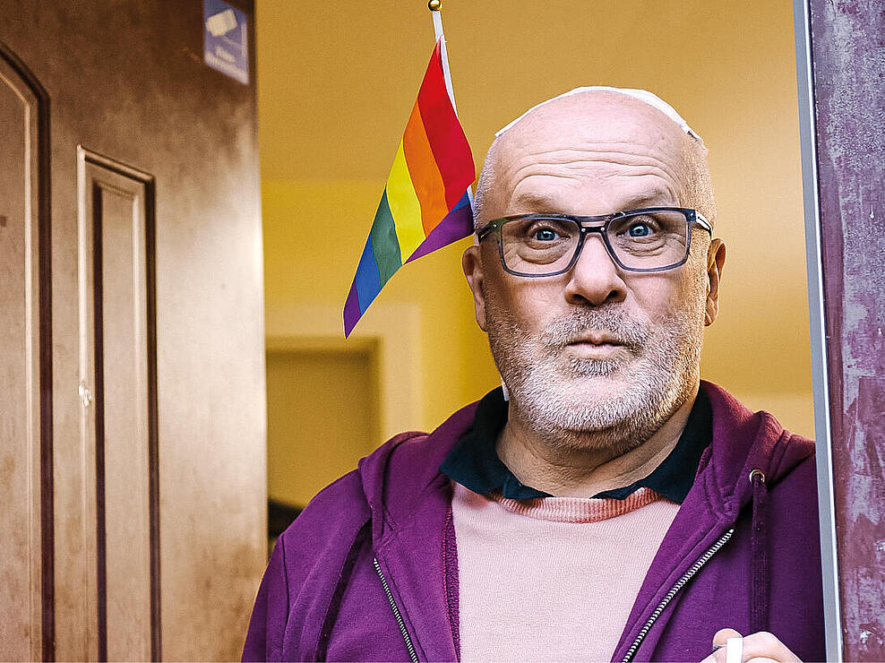 Andreas Otto in der Tür des House of Queers Berlin umgeben von Regenbogenflaggen