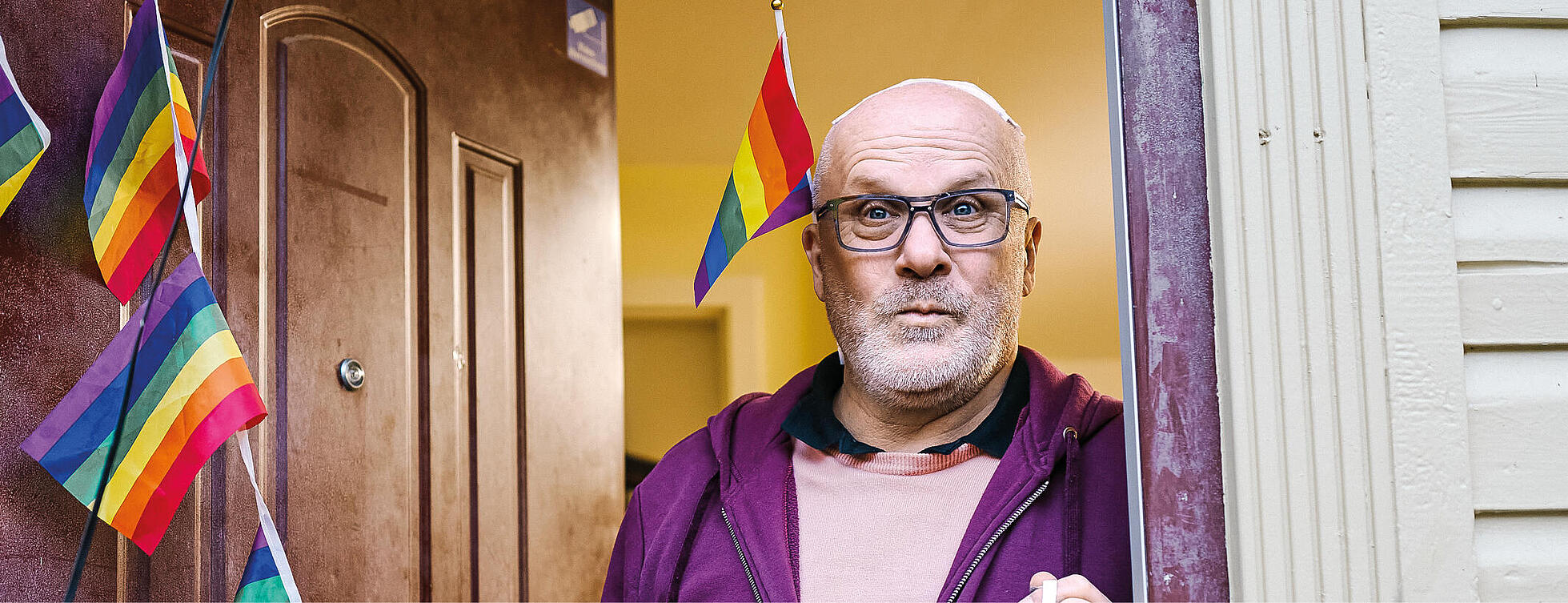 Andreas Otto in der Tür des House of Queers Berlin umgeben von Regenbogenflaggen