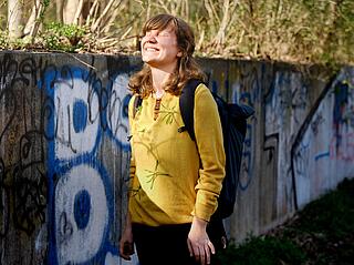 Wiebke Beushausen steht vor einer mit Graffiti bedeckten Mauer in Rosenthal-Lübars